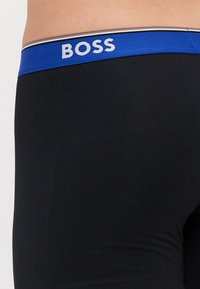 Crne bokserice s teksturiranim pojasom koji ima plavu traku. Na traci je natpis "BOSS" ispisan bijelom bojom, a uz to je naglašen zlatnom prugom.