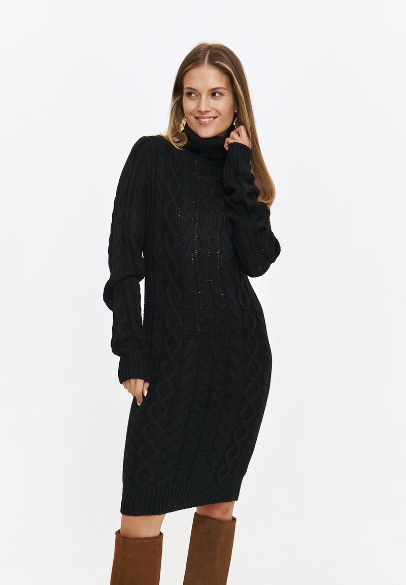 Dzianinowa czarna sukienka z wysokim kołnierzem, ozdobiona wzorem w warkocze, z prążkowanymi mankietami i dołem. Noszona z brązowymi kozakami do kolan. Miękka w dotyku.