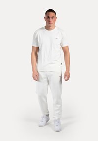 Camiseta blanca de algodón con mangas cortas y un pequeño logo en el pecho, combinada con pantalones de chándal blancos y zapatillas blancas.