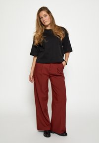 Črna kratka majica s krožnim izrezom, kombinirana z ohlapnimi, visoko pasnimi bordeaux hlačami. Gladka tekstura, minimalni detajli.