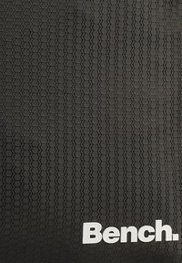 Zwarte textuuroppervlak met een hexagonaal patroon, met een opvallend wit logo dat "Bench" zegt.