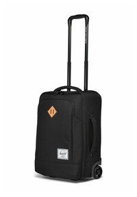 Valise à roulettes noire en matériau souple avec une poignée télescopique, une poche zippée à l'avant, une poignée latérale et un patch logo de Herschel Supply Company.