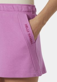 Falda de jersey de algodón rosa con un bolsillo lateral que presenta el logo bordado "HELLY HANSEN". El diseño incluye un corte relajado y un dobladillo.