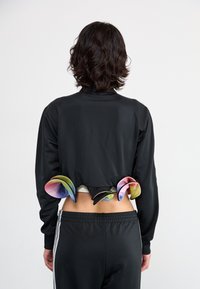 Veste noire courte à manches longues, featuring des accents colorés superposés à l'ourlet. Associée à un pantalon de sport noir avec une ceinture élastique.