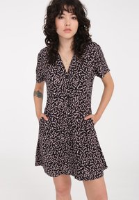 Kurzes, schwarzes Kleid mit pinkem, abstractm Muster, Knopfverschluss und Taschen. Hergestellt aus leichtem Stoff, mit taillierter Taille und weit schwingendem Rock.