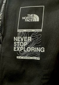 Felpa nera in cotone con logo bianco, testo che recita "NON SMETTERE MAI DI ESPLORARE" e linee di contorno con coordinate geografiche.