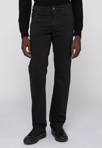 Pantalones negros de pierna recta, hechos de una tela de textura suave. Cuentan con bolsillos estándar y cierre de botón. Llevados con zapatillas negras.