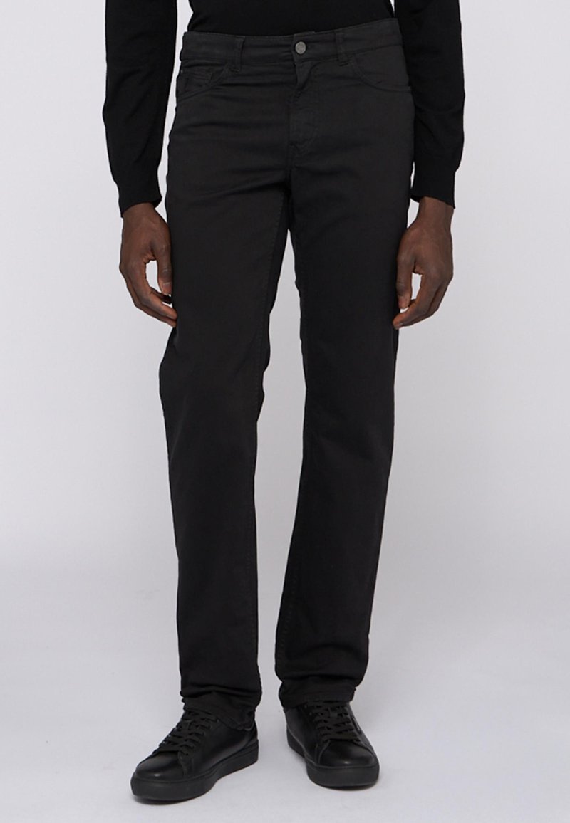 Pantalones negros de pierna recta, hechos de una tela de textura suave. Cuentan con bolsillos estándar y cierre de botón. Llevados con zapatillas negras.