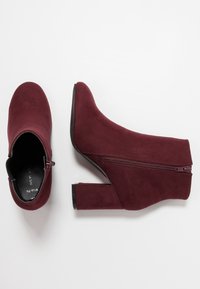 Par de botines de ante burdeos con tacones de bloque y cremalleras laterales sobre un fondo blanco.