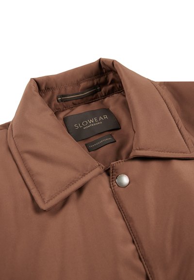 Bruine jas met een soepele textuur, puntkraag en drukknoopsluiting. Het label vermeldt "SLOWEAR MONTEDORO" met verzorgingsinstructies eronder.