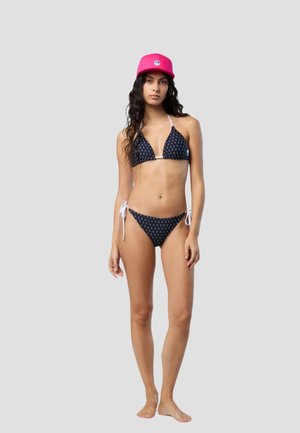 Bikini navy con stampa ancore bianche; top triangolare e slip con laccetti laterali. Abbinato a un berretto rosa brillante con un emblema.