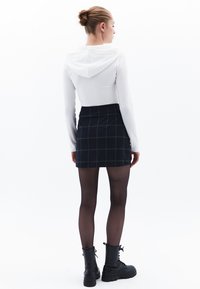 Top blanco de manga larga con capucha, combinado con una falda corta de cuadros negra. Botas negras hasta el tobillo. Medias y cabello recogido en un moño.