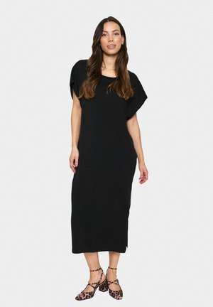 Black mid-length dress with a relaxed fit, short sleeves, and a round neckline. Worn with leopard print block-heeled shoes.