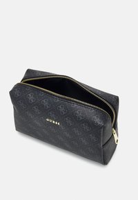 Trousse de maquillage noire en matériau texturé, ornée d'un motif de logo répétitif, d'une fermeture éclair dorée et du nom de la marque embossé à l'avant.