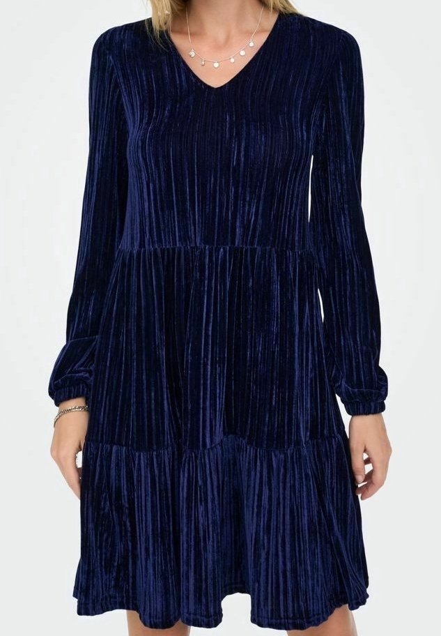 Femme portant une robe longue en velours bleu marine à manches longues avec un col en V et une jupe à étages, accessoirisée d'un collier et de bracelets.