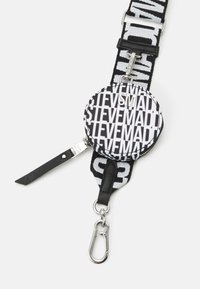 Μαύρη και λευκή κυκλική θήκη με φερμουάρ, με σχέδιο κειμένου "STEVE MADDEN", προσαρτημένη σε υφασμάτινη λαβή με μεταλλικό κλιπ και ρυθμιζόμενη αγκράφα.