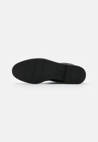 Suela de zapato de goma negra con patrones texturizados, que presenta ranuras horizontales y una forma redondeada. Logo de la marca y indicación de talla claramente visibles.