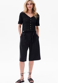 Czarna dzianinowa bluzka z krótkimi rękawami i drewnianymi guzikami, w połączeniu z luźnymi czarnymi kulotami z bocznymi kieszeniami i wiązaniem w talii.