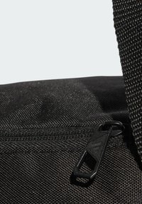 Borsa nera in nylon con superficie testurizzata, chiusura con cerniera e tracolla in rete. Dettagli notevoli includono un elegante cursore dalla forma geometrica.