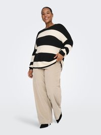 Mustvalgete triipudega kampsun pikkade varrukatega, sobitatud laia beeži kirju püksidega ja mustade kontsadega. Pehme tekstuur, lõdvestunud lõige.