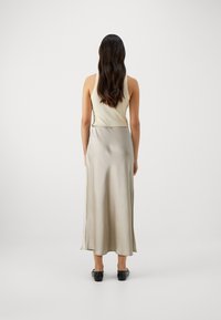 Robe midi sans manches en soie crème avec une texture lisse, dotée d'une fente latérale et d'un éclat subtil, accompagnée de chaussures noires.