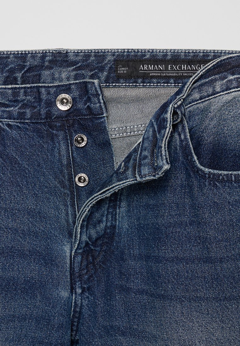 Granatowe dżinsy z denimu z trzema widocznymi metalowymi guzikami oraz czarną metką Armani Exchange wewnątrz pasa.