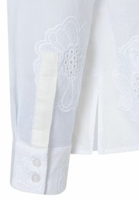 Witte shirt met geborduurde bloemenpatronen, knoopmanchet details en een rechte snit met zijsplitten. Gemaakt van een lichte stof.
