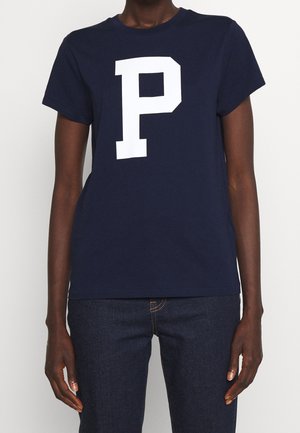 Marineblaues Baumwoll-T-Shirt mit großem weißem "P"-Motiv auf der Brust, kurzen Ärmeln und Rundhalsausschnitt. Kombiniert mit dunklen Jeans.