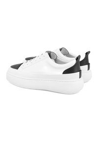 Witte leren sneakers met een zwarte neus en hakaccent. Dikke witte rubberen zool, ronde veters en een gladde textuur.