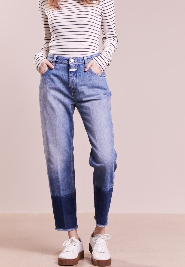 Femme portant un jean bicolore bleu clair avec des revers bleu foncé, des baskets blanches et un haut blanc à manches longues avec des rayures horizontales noires.
