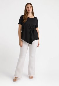 Top nero a maniche corte con dettaglio a nodo laterale, abbinato a pantaloni bianchi a palazzo. Tessuto liscio, vestibilità comoda e scollatura rotonda.