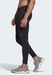 Black athletic leggings with a fitted design, featuring mesh panels and a subtle logo. Worn with gray running shoes and a zippered hem.