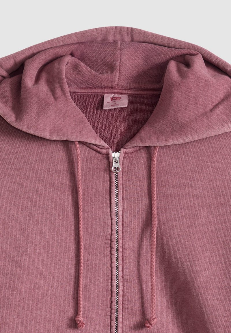 Lila ritsvest met capuchon, ritssluiting aan de voorkant en bijpassende trekkoorden, met een zachte textuur en een voering van fleece aan de binnenkant.