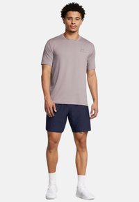 Light brown athletic t-shirt with short sleeves and a subtle logo, paired with dark navy shorts. Footwear is white sports shoes.