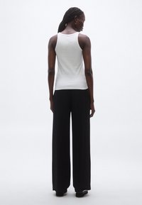 Fehér, testhez simuló ujjatlan felső, fekete, bő szabású nadrággal párosítva. Sima textúrájú; mintázat vagy feltűnő kiegészítő nem látható.