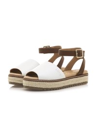 Sandalias blancas de puntera abierta con una correa marrón en el tobillo, que presentan una suela en forma de cuña estilo yute y una suela exterior de goma texturizada para mayor agarre.