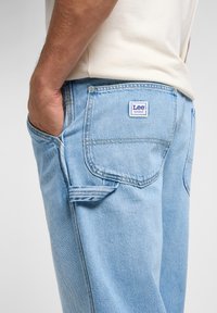 Vaqueros de mezclilla azul claro con un corte clásico, que presentan un distintivo parche del logo de Lee en el bolsillo trasero y detalles de costura sutiles.
