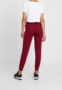 Burgundyröda sweatpants med elastiskt midjeband och mudd. I kombination med en enkel vit t-shirt och svarta träningsskor. Enkelt, avslappnat design.