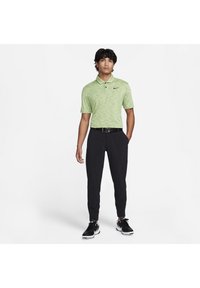 Zöld mintás pólóing gallérral, fekete slim-fit nadrággal és fekete sportcipővel párosítva, a pólón a Nike logóval.