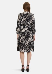 Svart blommig klänning med långa ärmar, åtsittande midja och flödande nederdel. Har ett vitt botaniskt mönster; bärs med svarta klacksandaler.
