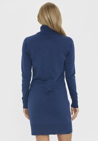 Tamno plava haljina s turtleneck izmešane meke pletene tkanine, s dugim rukavima i oblikovanim siluetom, završava iznad koljena s rebrastim detaljima.