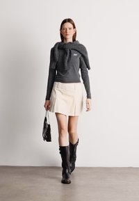 Γκρίζα μπλούζα με μακριά μανίκια, κρέμα μίνι φούστα και μαύρες μπότες μέχρι το γόνατο, με ένα γκρίζο πουλόβερ ριγμένο στους ώμους και μια μαύρη τσάντα.