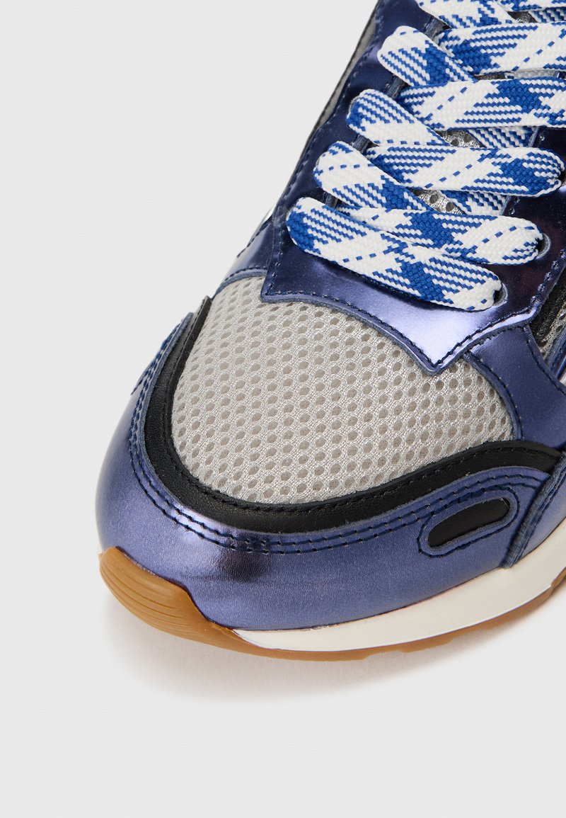 Sneaker mit oberer Fläche in metallischem Blau, Mesh-Details, schwarzen Akzenten und blauen, diamantmusterigen Schnürsenkeln. Gummisohle mit hellbraunem Boden.