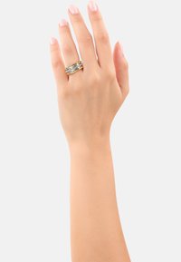 Gouden en zilveren ring gedragen aan een hand, met gelaagde banden en textuuraccenten. De vingernagels zijn natuurlijk, met een lichtroze glans.