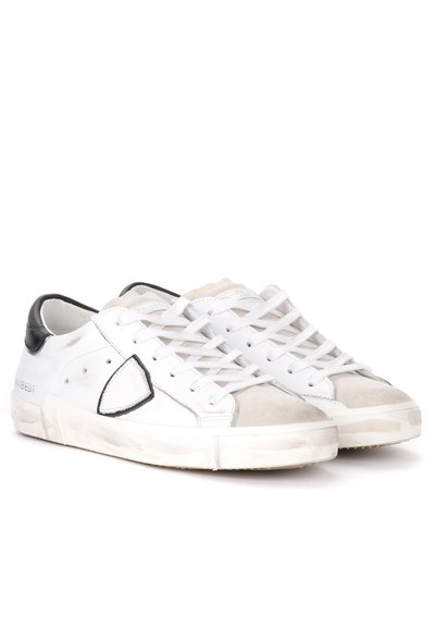 Sneaker bianche in pelle con dettagli neri, punta in suede, lacci piatti e suola texturizzata. Presenta un logo triangolare sul lato.