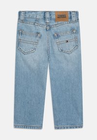 Light blue denim jeans with a straight cut, featuring a brown leather patch labeled "TOMMY HILFIGER" and two back pockets with stitching.