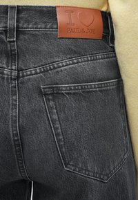 Črni jeans iz jeansa z usnjenim oznako "I ❤️ PAUL & JOE." Lastnosti vključujejo zadnji žep in šivane detajle.