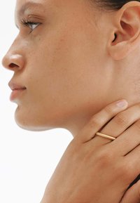 Anillo texturizado en oro llevado en una mano, con una vista cercana de la mano descansando contra el cuello, mostrando un tono de piel suave y detalles sutiles.