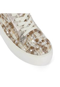 Sneaker met een textuurstof in off-white met bruine accenten, versierd met glanzende pailletten en een metallic zilveren tong met witte veters.