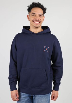 Sweatshirt bleu marine avec capuche, poche avant et détails brodés de fleurs orange et bleues sur le côté gauche de la poitrine. Matière en coton doux.